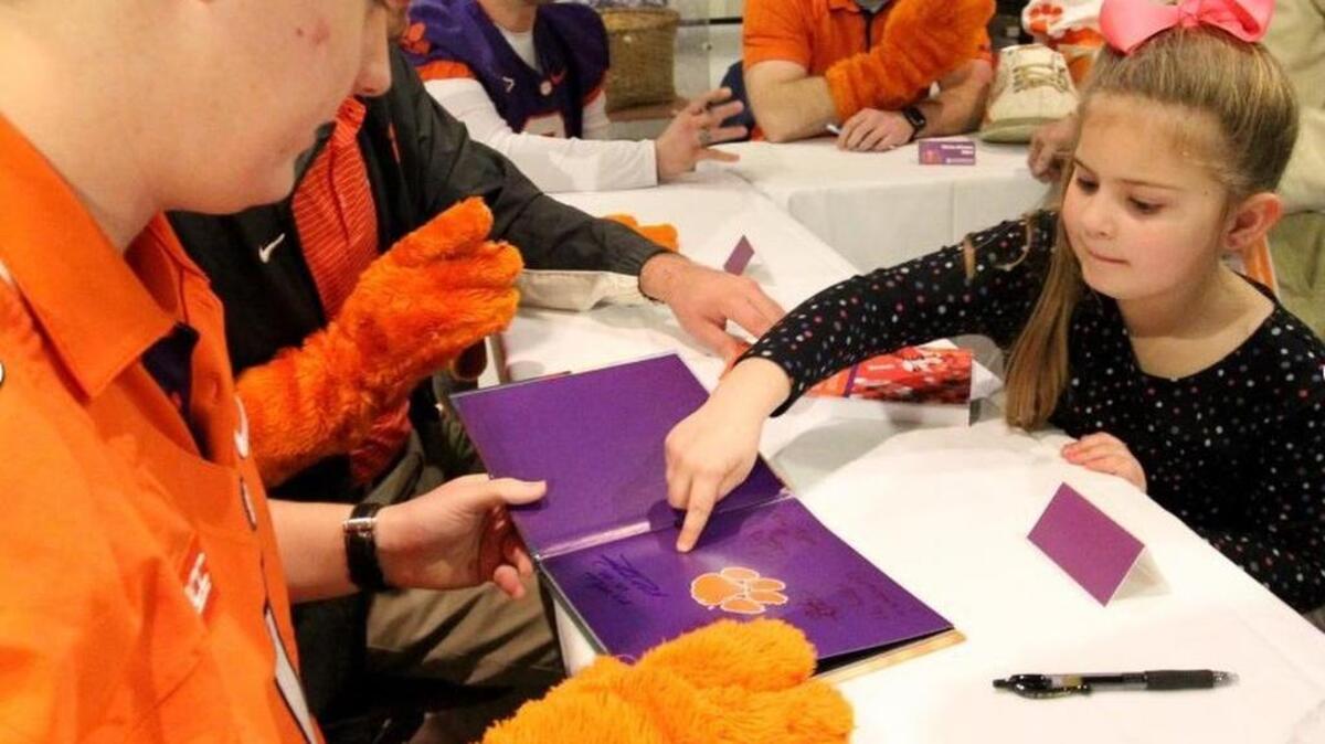 Mattison Voigt, 6, of Anderson, shows Andrew Beeler where she wants his autograph on a book at the Anderson County Museum on Tuesday. Beeler and several other former Clemson Tiger mascots were on hand to greet fans during a book signing for John Seketa’s new book “Clemson Through the Eyes of the Tiger.”