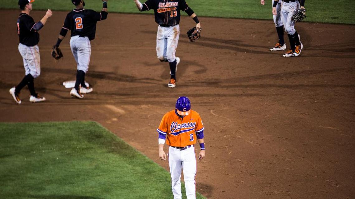 Clemson's Chase Pinder walks off the field as Oklahoma State players celebrate their win over Clemson on Saturday. The Cowboys defeated the Tigers again on Sunday to win the Clemson Regional.
