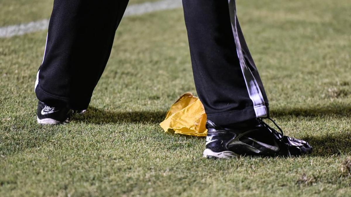 A yellow penalty flag sits at the feet of a referee.