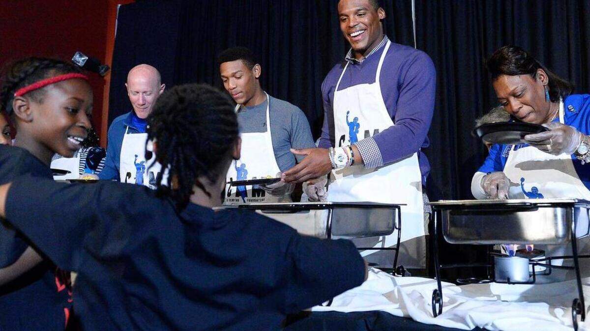 Cam Newton, in center, with his family members Jackie (mother), on right, younger brother Caylin on left, serve a traditional Thanksgiving meal to kids as two young girls dance for Cam in line, during Cam Newton Foundation's "Cam's Thanksgiving Jam" . The panthers quarterback along with members of his family and more than 50 volunteers served up a traditional Thanksgiving meal for 800 underprivileged kids held at The Fillmore on Nov. 23,2015.