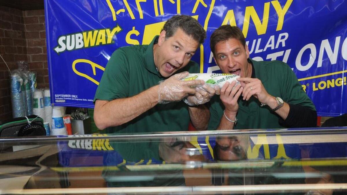 Famous fans Mike Golic, left, and Mike Greenberg, of ESPN, pose behind the counter at a SUBWAY restaurant in New York.